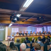 Diretor odir discursando com a mesa de autoridades e o público assistindo.